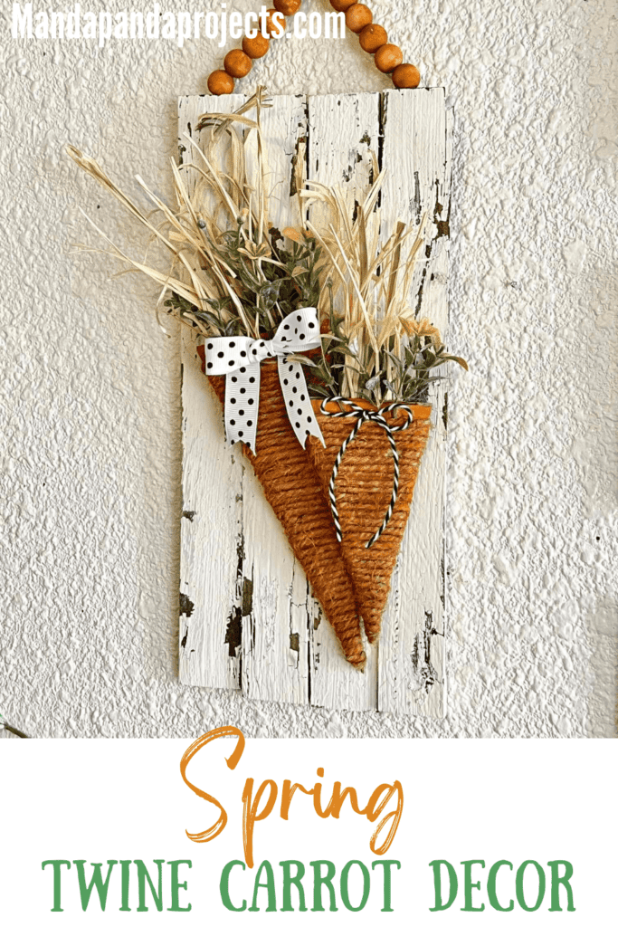 Spring cardboard carrot craft made with a twine wrapped carrot on a white chippy background and a wood bead hanger for DIY Easter decor
