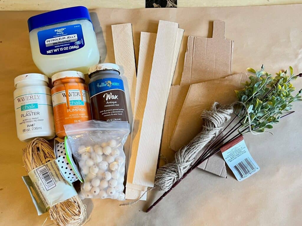Supplies needed to make a spring carrot craft with cardboard and twine on wooden shims.