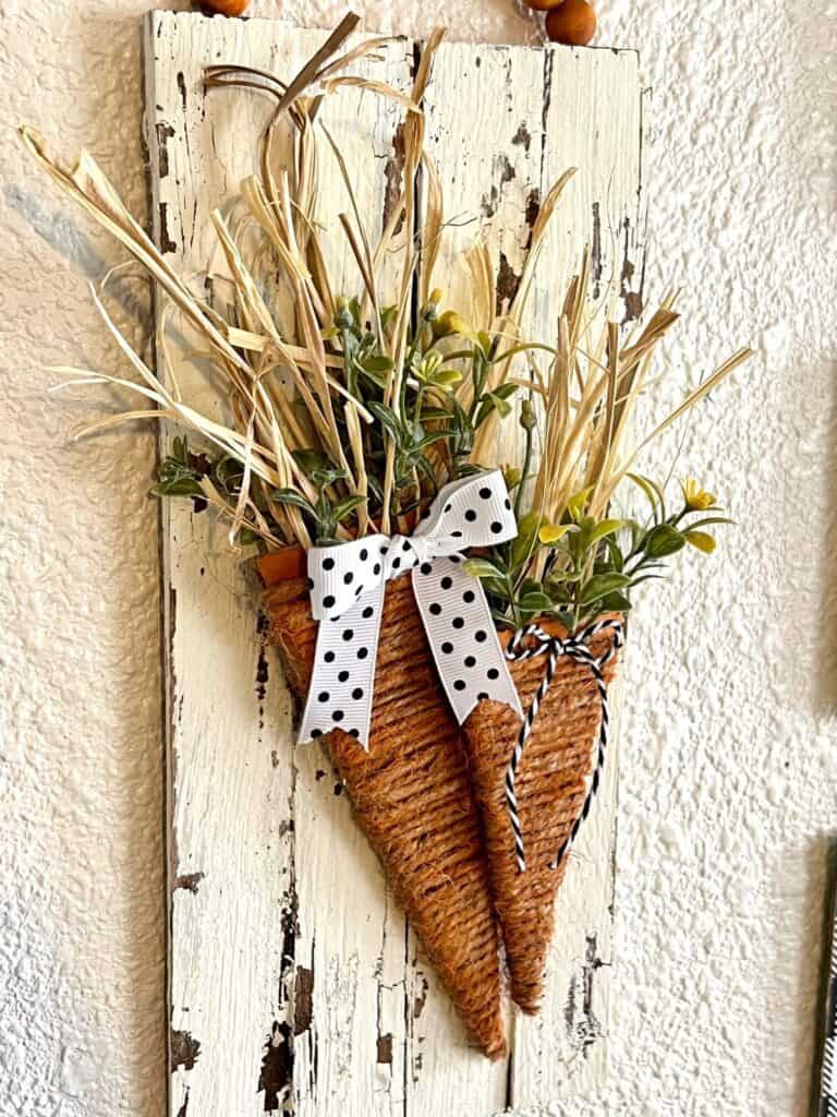 Spring cardboard carrot craft made with a twine wrapped carrot on a white chippy background and a wood bead hanger for DIY Eastet decor