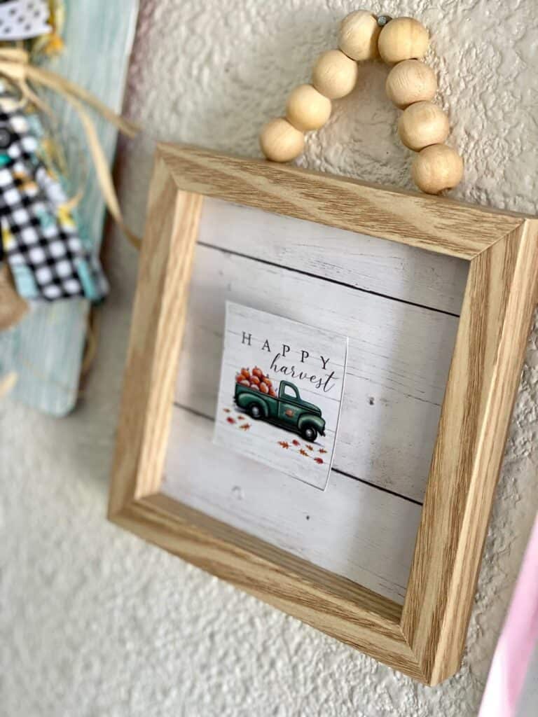 Small wooden frame with wood bead hanger and faux shiplap background and Dollar Tree back of the calendar mini "Happy Harvest" truck.