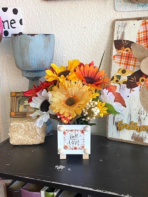 Dollar Tree "fall in love" back of the calendar mini print with a mixed sunflower bouquet on a bookshelf with other fall crafts and decor.
