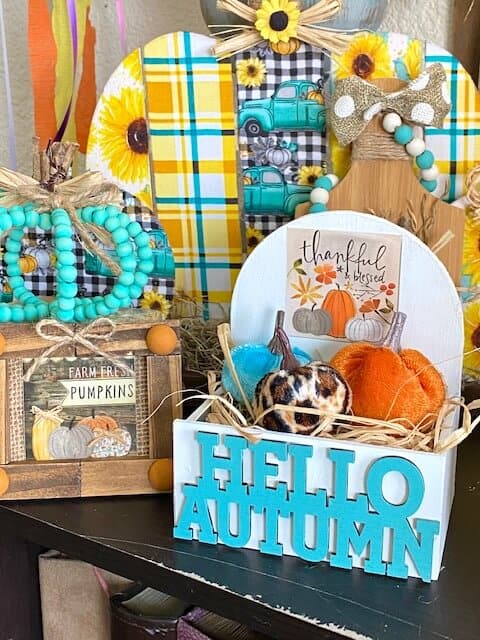 Dollar Tree Hello Autumn mini tiered tray pumpkin crate with the Dollar Tree "Thankful and Blessed" print from the back of the calendar next to other fall projects on a bookshelf.