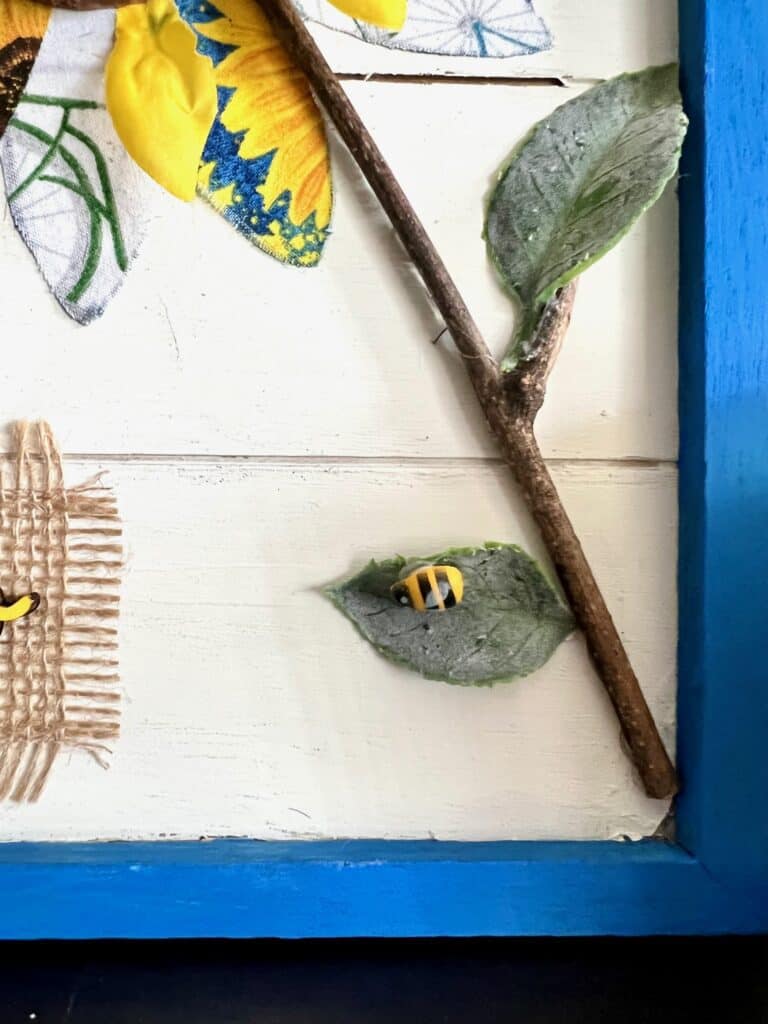 Wooden stick form outside as the stem of the fabric sunflower with little bumble bees and faux green leaves.
