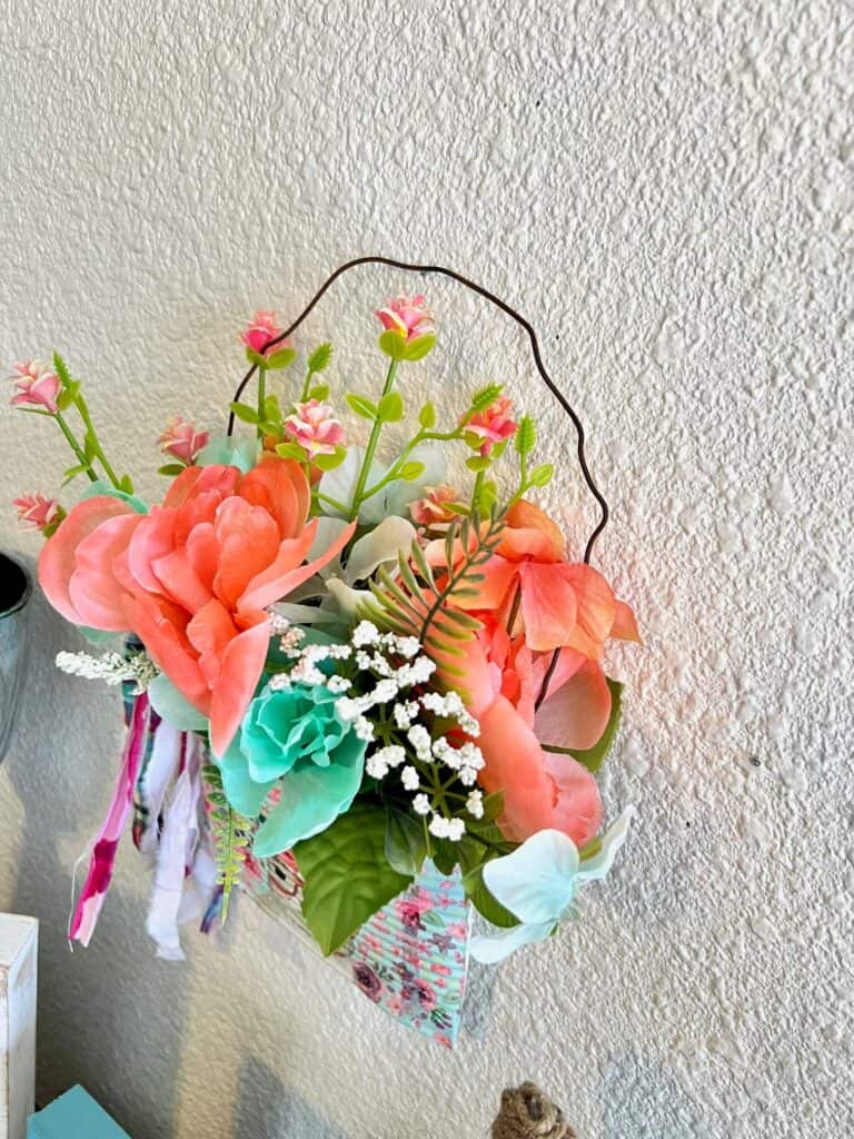 Close up of the flowers used in the Spring and Easter smashed can DIY decor, mint and coral colors with a shaggy fabric bow tied around the rusty wire hanger.