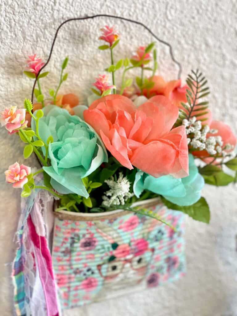 Close up of the flowers used in the Spring and easter smashed can DIY decor, mint and coral colors with a shaggy fabric bow tied around the rusty wire hanger.