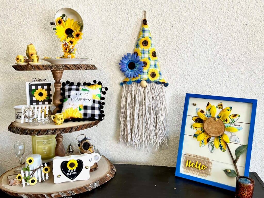 DIY Dollar Tree Sunflower Gnome next to a blue and yellow fabric sunflower and a 3 tiered tray decorated with Sunflower and Bee decor.