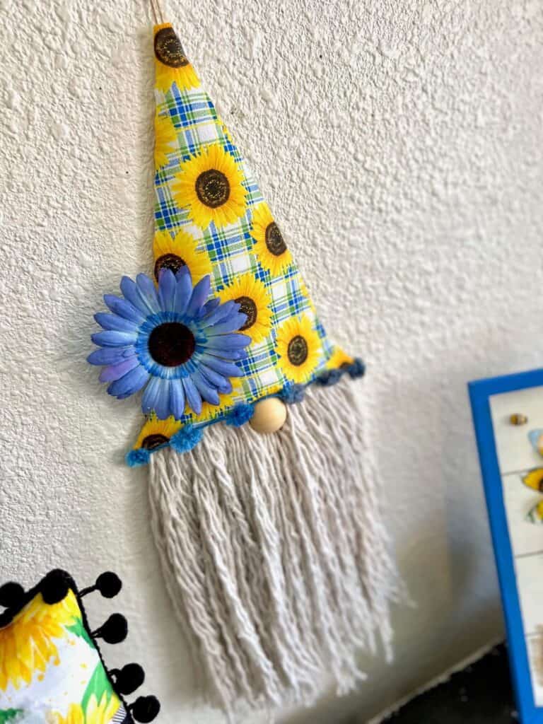 Dollar Tree DIY Sunflower Gnome Makeover with blue and yellow Walmart sunflower fabric and a Dollar Tree Mop Head string beard with a blue sunflower.
