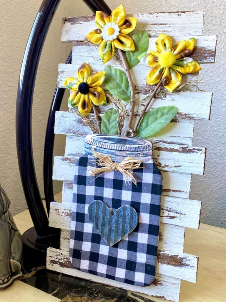 DIY Fabric Sunflower Mason Jar decor with buffalo check fabric and wooden shims on a chippy paint background. for spring and summer crafty decor.