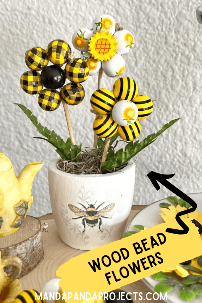 DIY Wood Bead Flowers made with sunflower and bee wood beads in a mini terra cotta pot with a napkin decoupaged and sitting on top of a tiered tray as summer decoration.