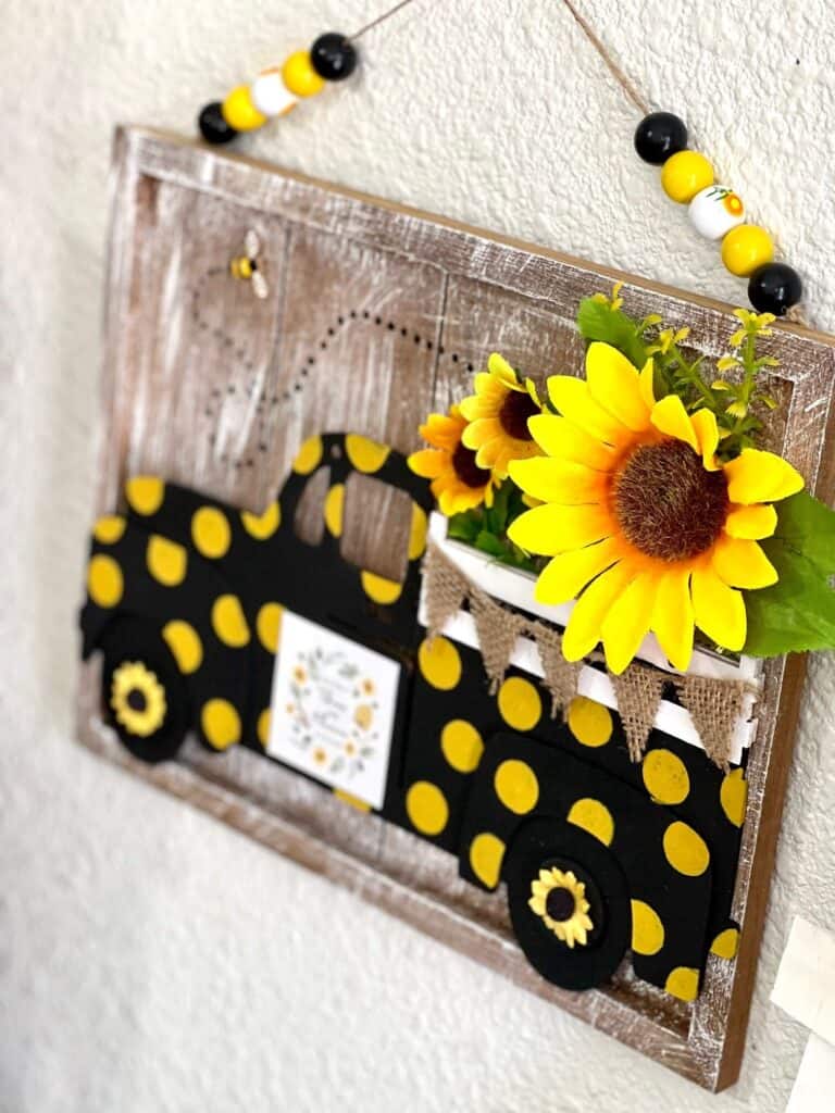 DIY Dollar Tree Sunflower Truck made with Dollar Tree supplies, faux sunflowers, a honey bee, wood bead hanger, and black with yellow polka dots for spring and summer DIY affordable decor.