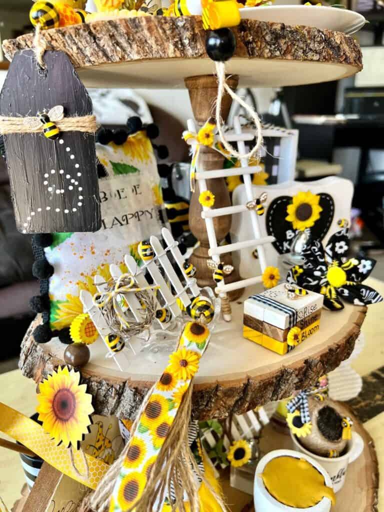 Left side of the middle tier of the tray showing the Mini sunflower fence, the sunflower wood bead garland and the small Bee Happy pillow.