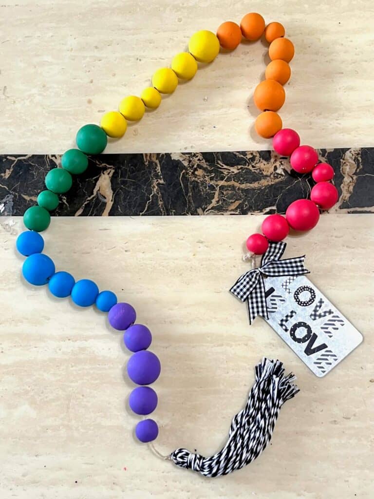 DIY Rainbow Wood Bead Garland to craft, decorate, and celebrate summer or pride month in June. With a "love is love" hang tag and a handmade black and white tassel.