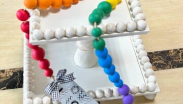 DIY Rainbow Wood Bead Garland to craft, decorate, and celebrate summer or pride month in June. With a "love is love" hang tag and a handmade black and white tassel.