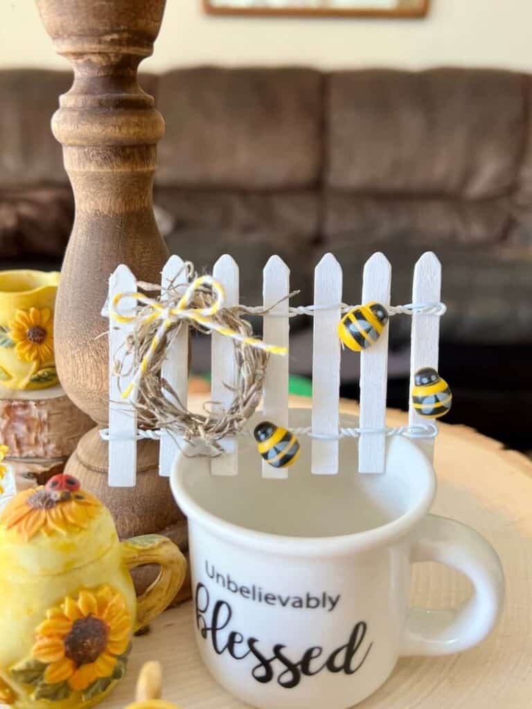 Small white picket fence decor with a mini wreath and yellow bow and small bumblebees.