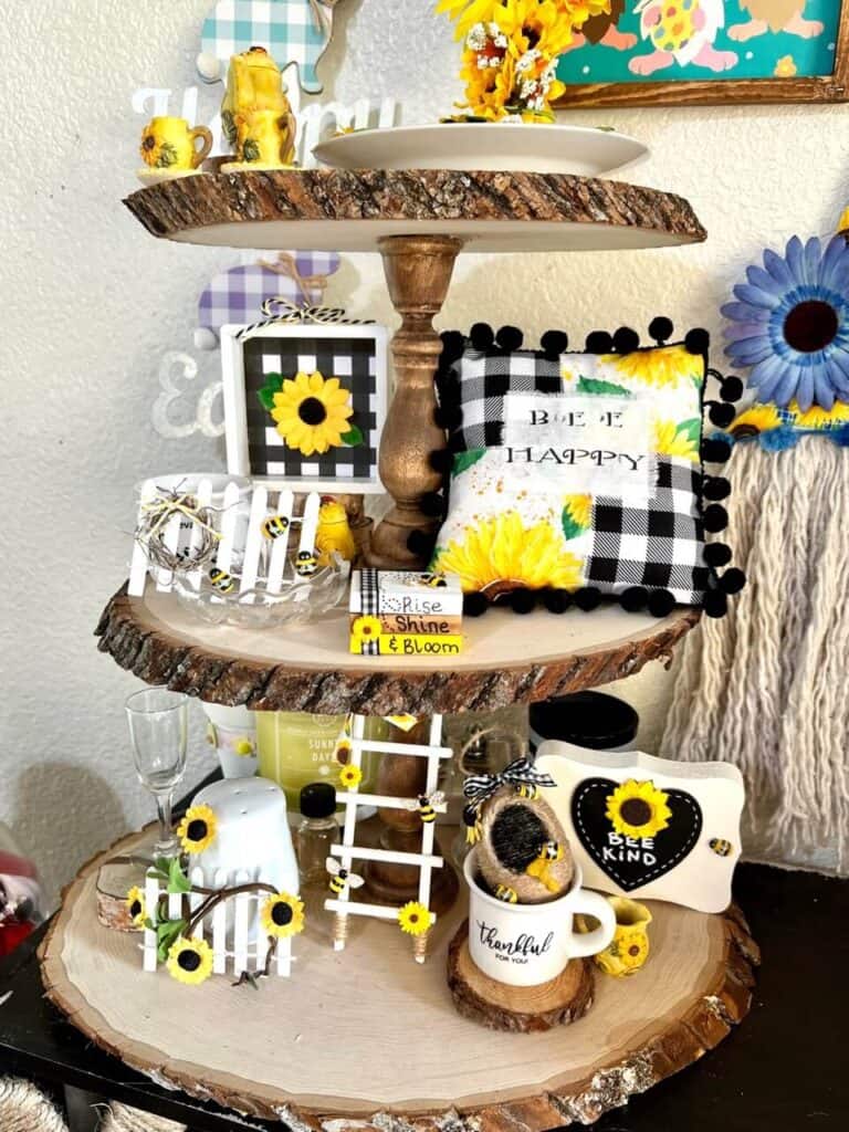 Rustic wooden round tiered tray filled with sunflower and bumblebee crafts and decor, including the white picket fences that are in this blog post.