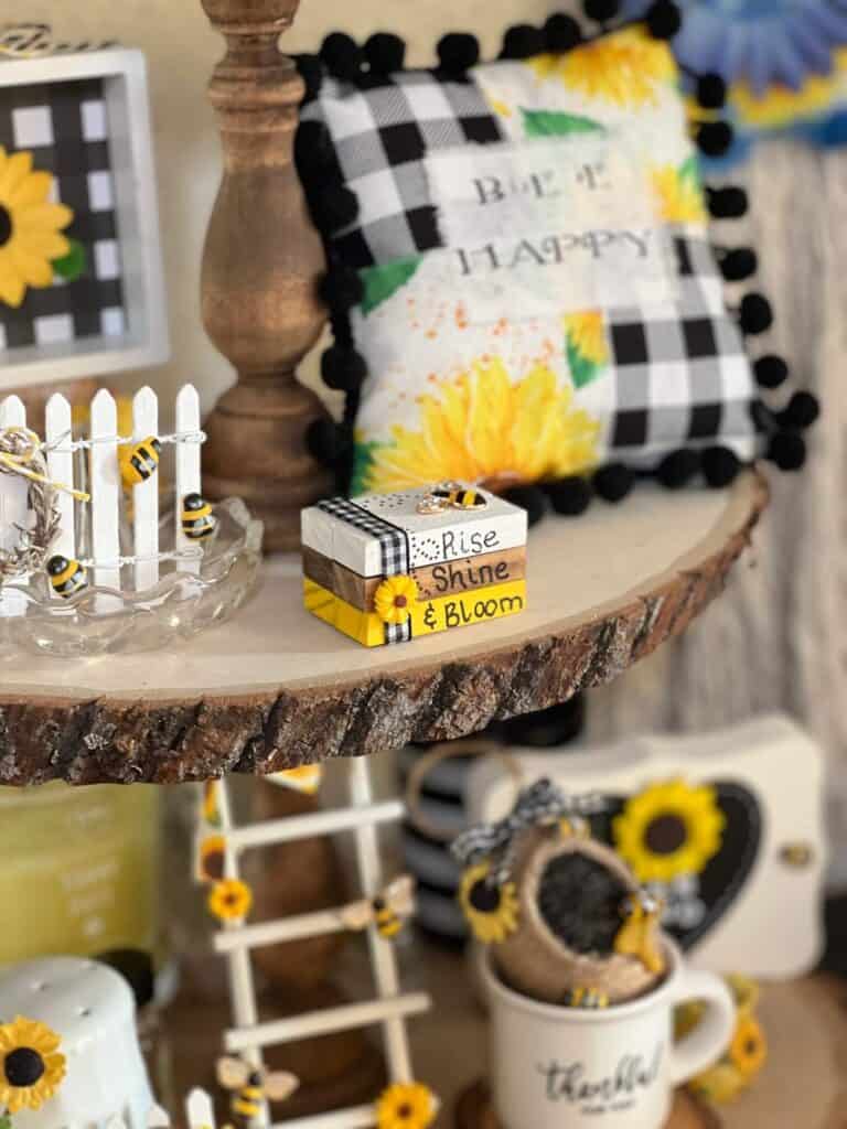 Front of the mini bookstack decor showing the words Rise Shine & Bloom, with buffalo check ribbon and a mini sunflower.
