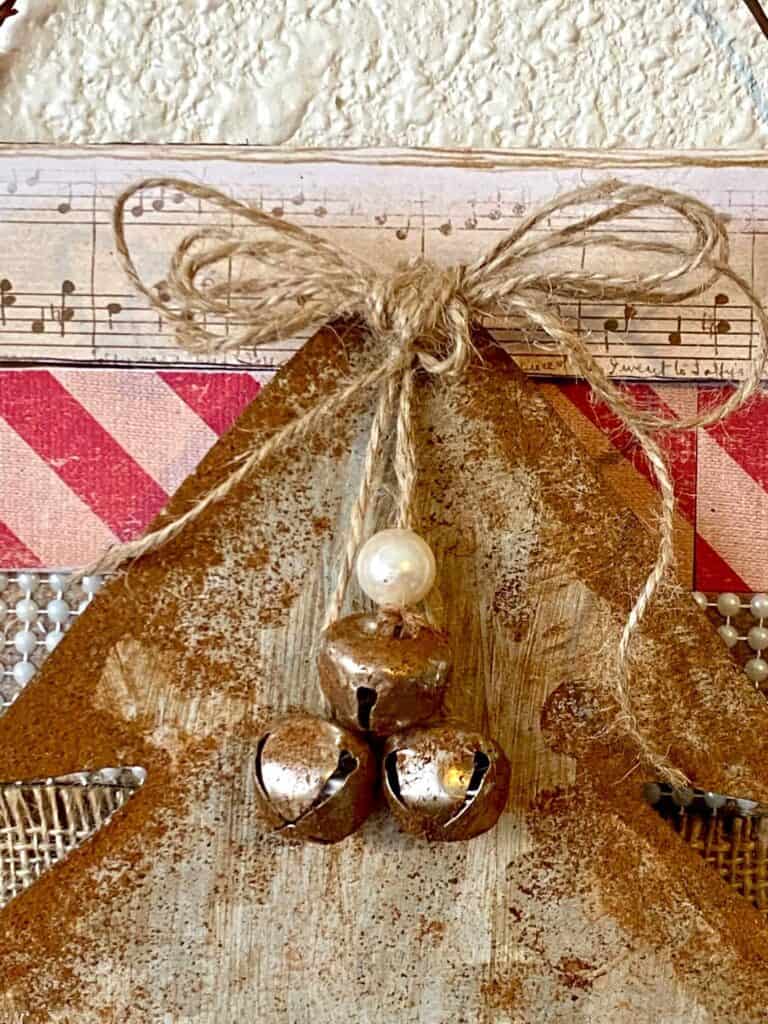 Twine bow with hanging rusted silver bells and a pearl bead at the top of the galvanized metal christmas tree.