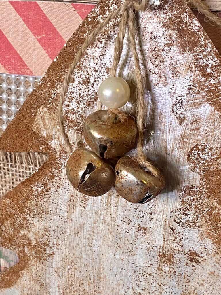 Small silver bells looking rusty hanging from a piece of twine with a pearl bead.