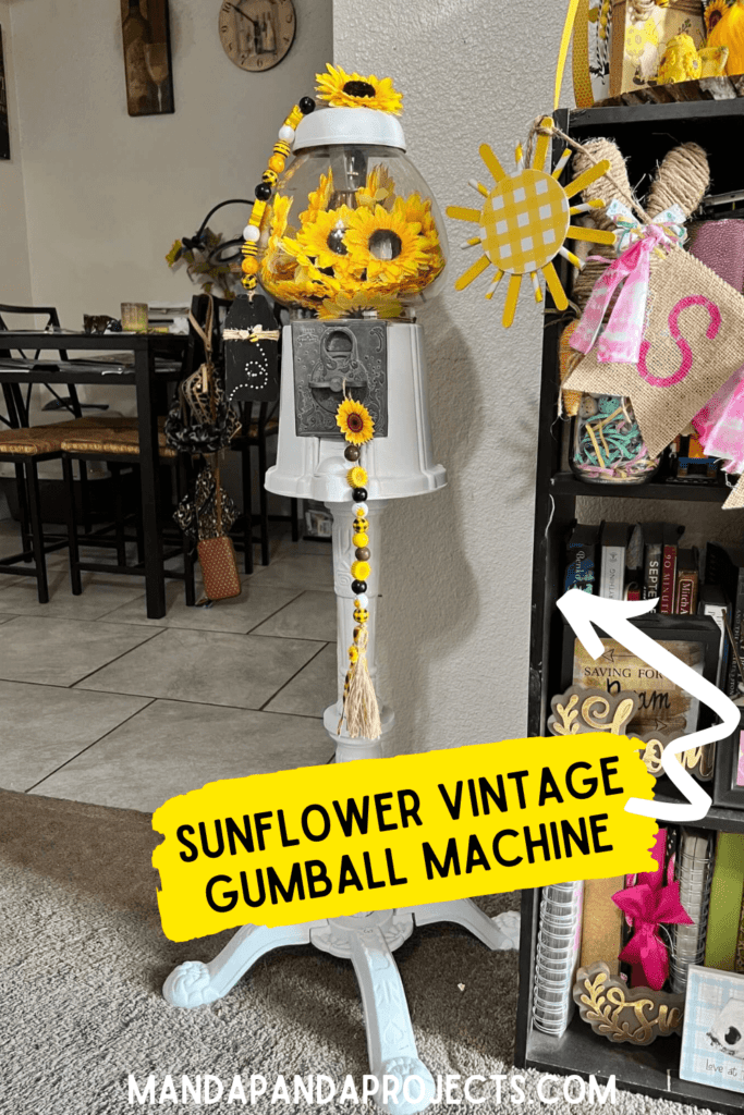 Sunflower Vintage Gumball Machine with sunflower heads inside and on top, and sunflower and bee mini wood bead garlands hanging form the top and coin turner. Gumball machine is painted all white.