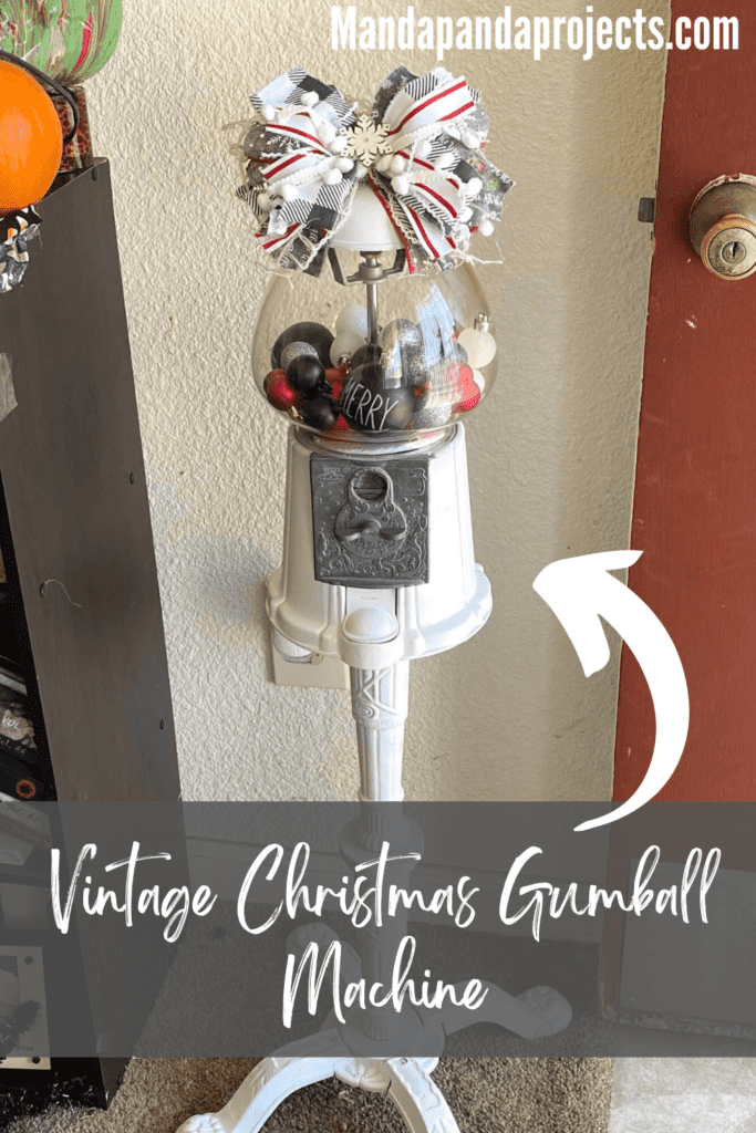 Christmas decorated thrift store vintage gumball machine that is painted white, with red, black, silver, and white ornament bulbs inside and a big messy bow on top.