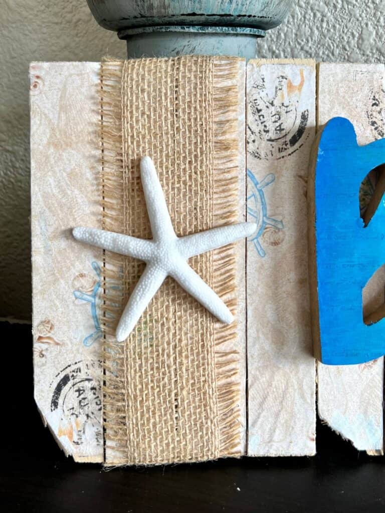 A dollar Tree starfish glued to a strip of burlap to the left of the wooden word beach.