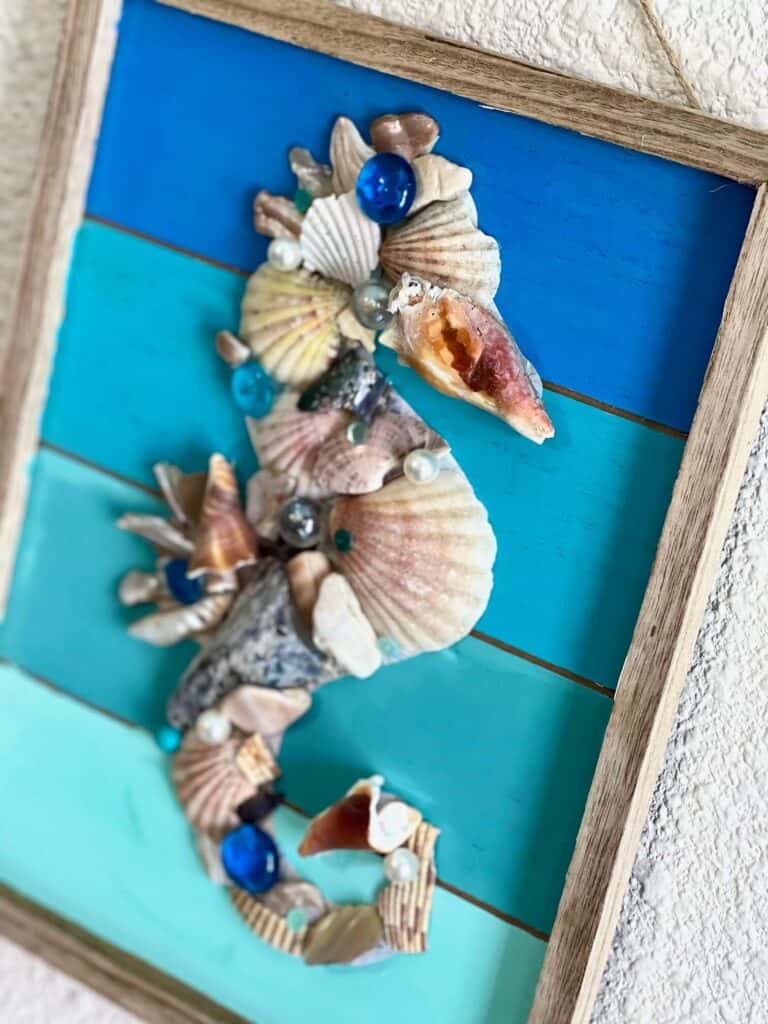 Ombre blue and teal background with a seahorse made out of seashells and pearls and marbles for DIY decor for a summer nautical, coastal, beach house.