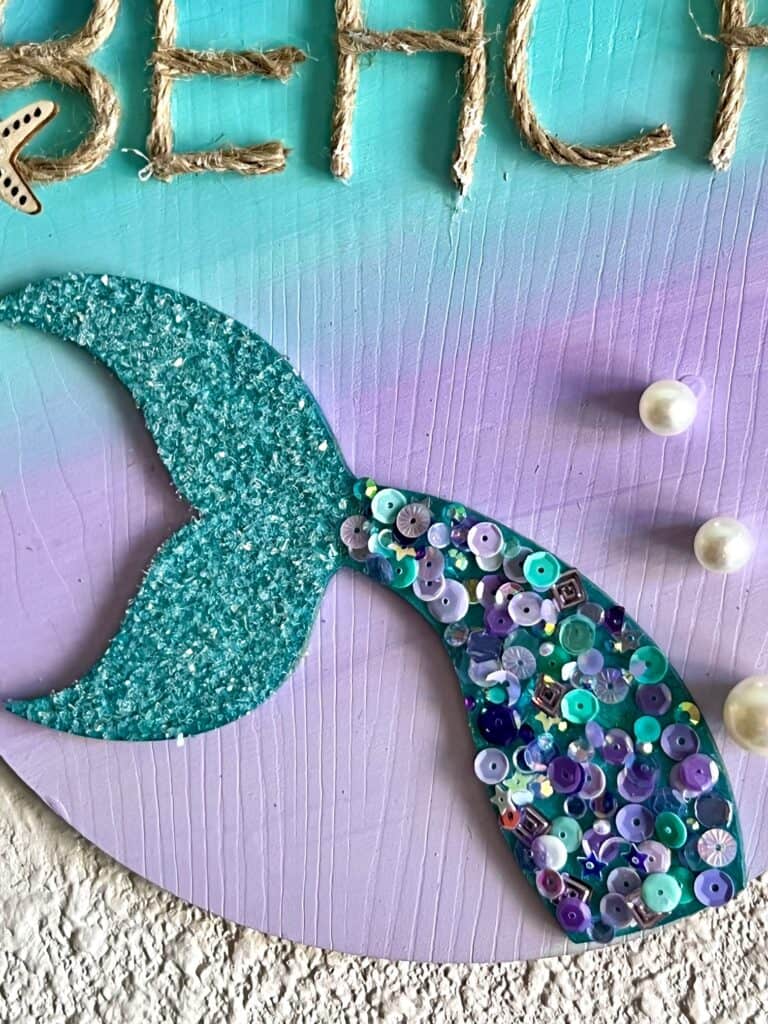 Wooden mermaid tail painted metallic teal with purple, teal, and blue sequins and diamond dust in the fin, along with pearl bead "bubbles".