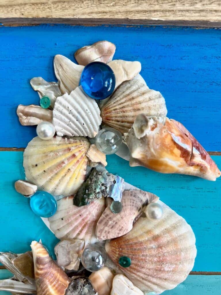 Top portion and head of the seahorse made out of seashells, marbles, pearls, and sequins.