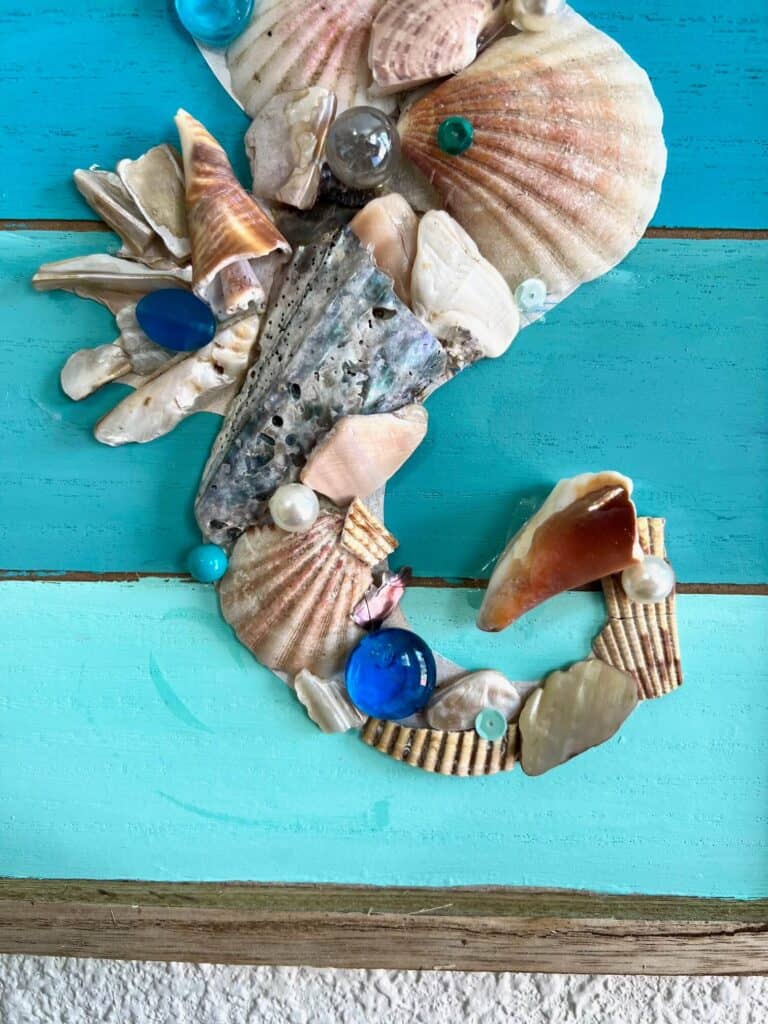 Bottom portion and tail of the seahorse made out of seashells, marbles, pearls, and sequins.