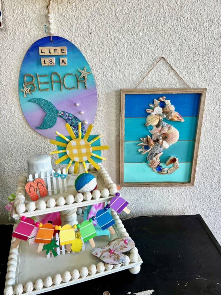 Dollar Tree ombre mermaid tail project next to a seashell seahorse and a fun in the sun tiered tray on a bookshelf.