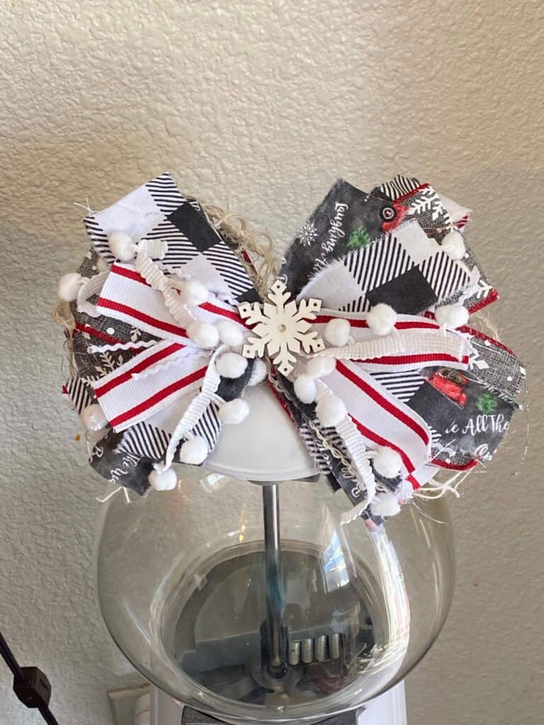 Big messy bow with a snowflake in the center on top of the white painted vintage gumball machine.