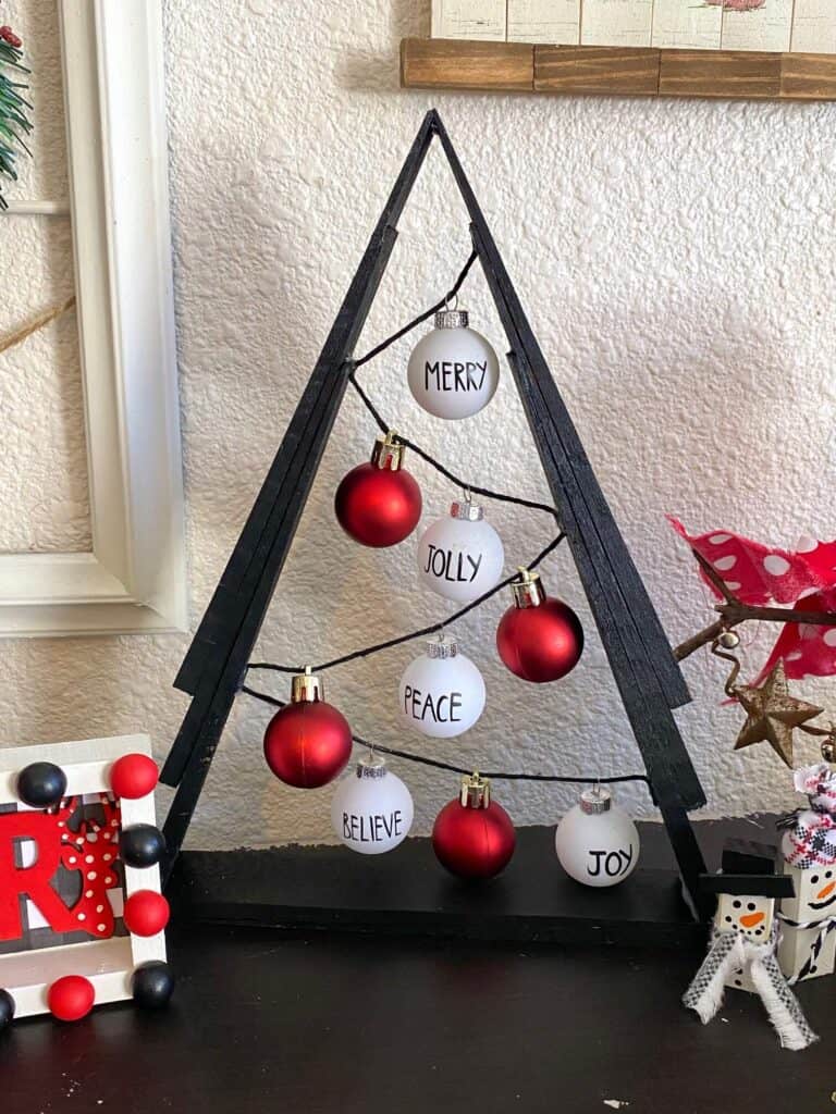 Black A frame wooden shim Christmas Tree with small red and white Rae dunn inspired bulb ornaments on black string.