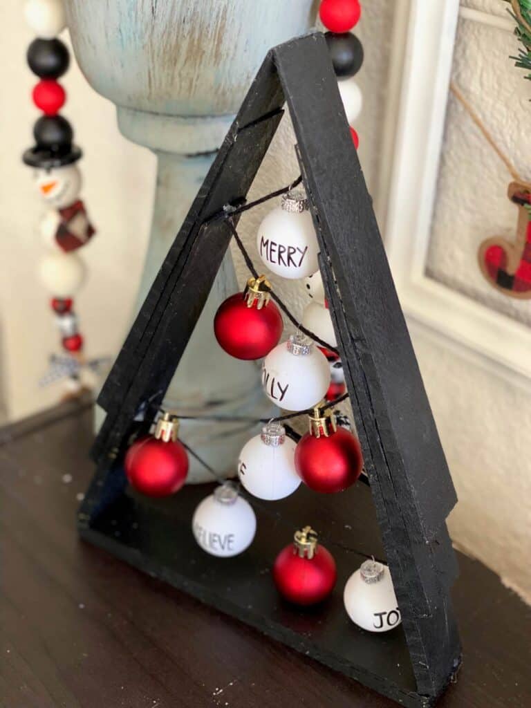 Black A frame wooden shim Christmas Tree with small red and white Rae dunn inspired bulb ornaments on black string.