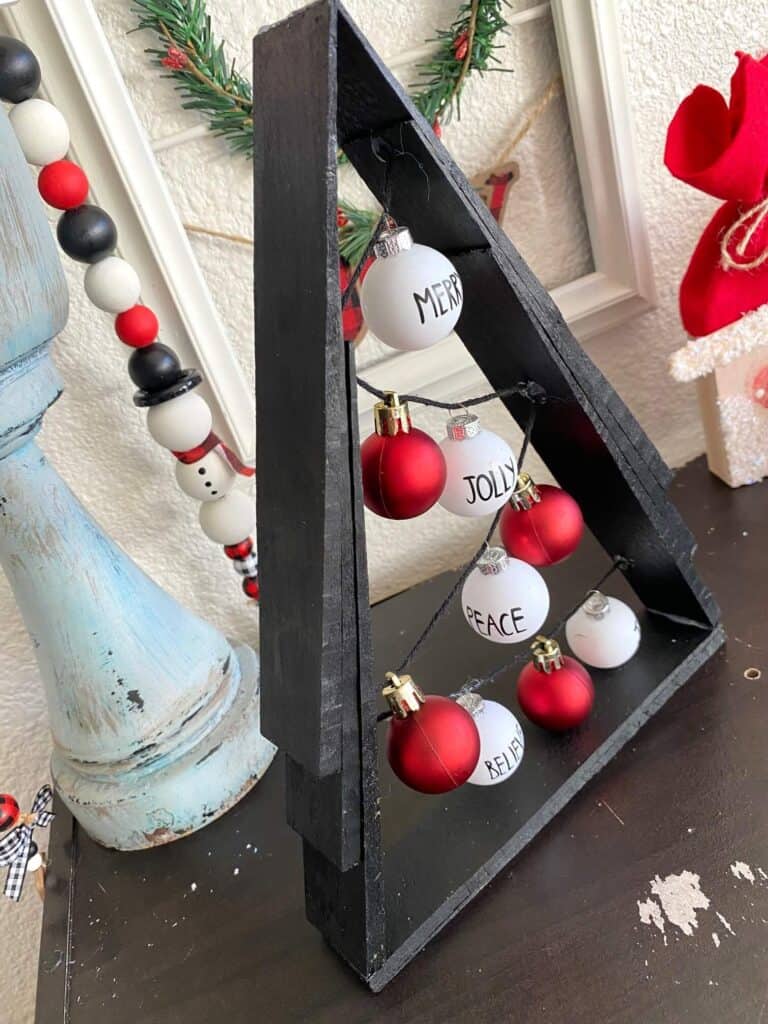 Black A frame wooden shim Christmas Tree with small red and white Rae dunn inspired bulb ornaments on black string.