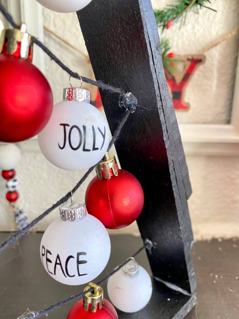 Close up of the black string hot glued to the inside of the Christmas tree frame with a Christmas ornament bulbs that say "Jolly" and "Peace"