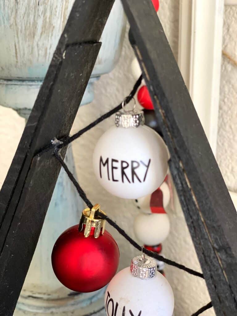 Close up of the top of the Christmas Tree wooden decor with a small white bulb ornament that says "Merry" in Rae Dunn inspired letters.