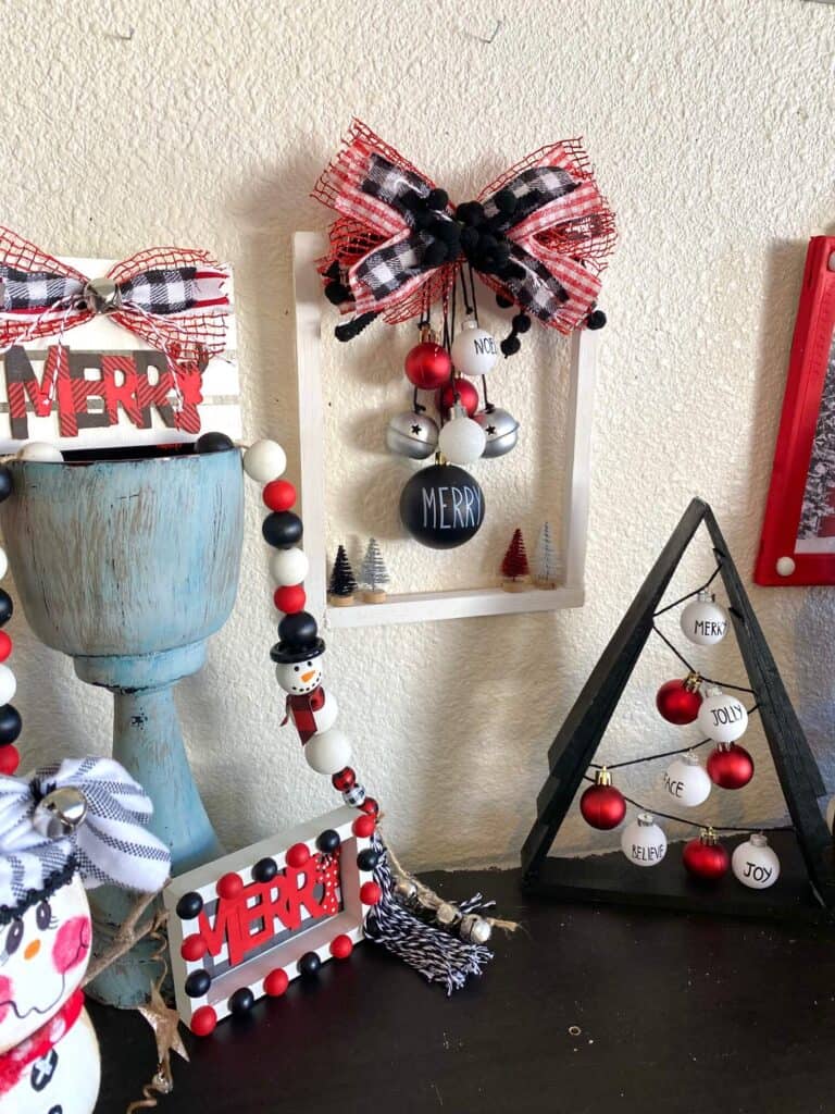 Red white and black themed christmas crafts and decorations all set up on a book shelf, along with the A frame wooden shim christmas tree that is featured in this blog post.