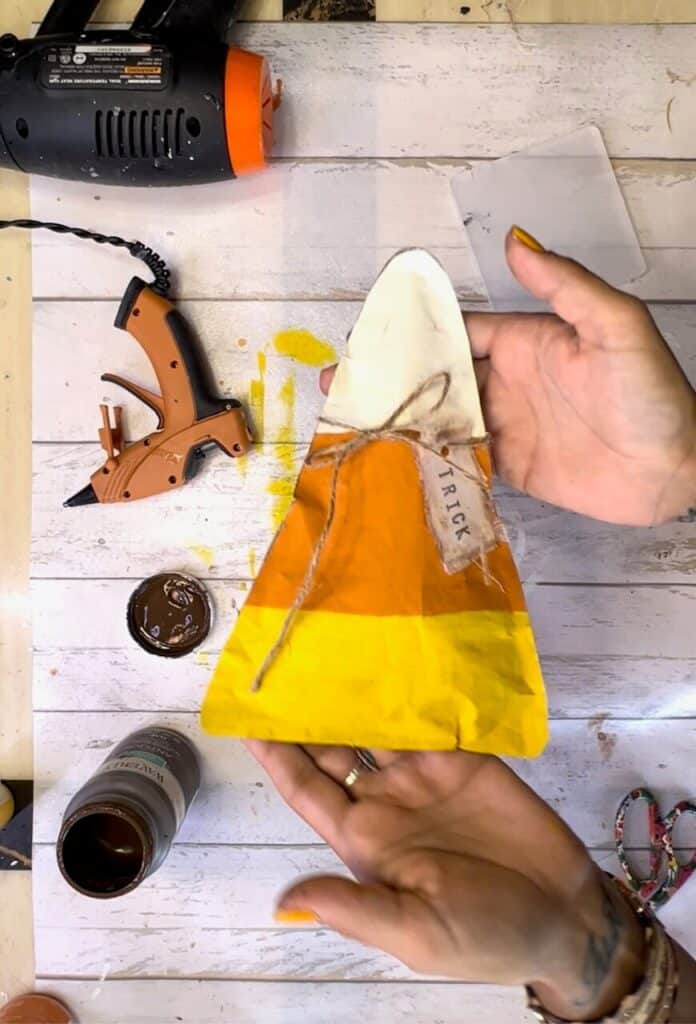 Tie the white fabric hangtag that says "trick" around the top of the candy corn with twine.