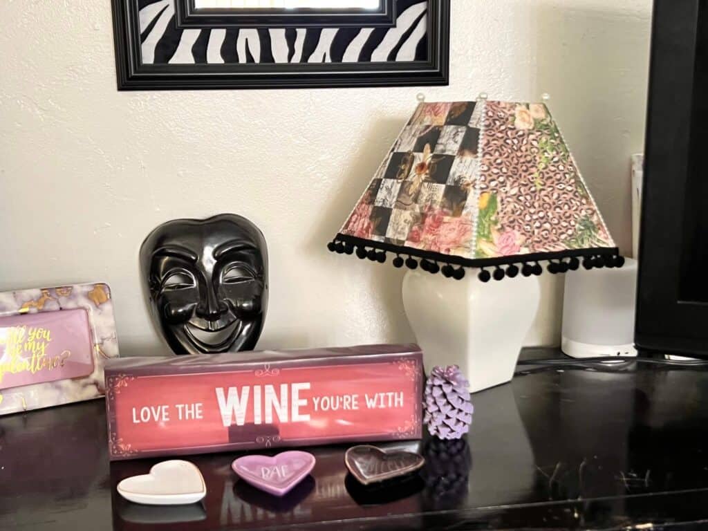 Thrift Store Lamp Flip, the completed project sitting on a bookshelf with e Drama face, a "love the wine your with" shelf sitter and a Zebra mirror on the wall.