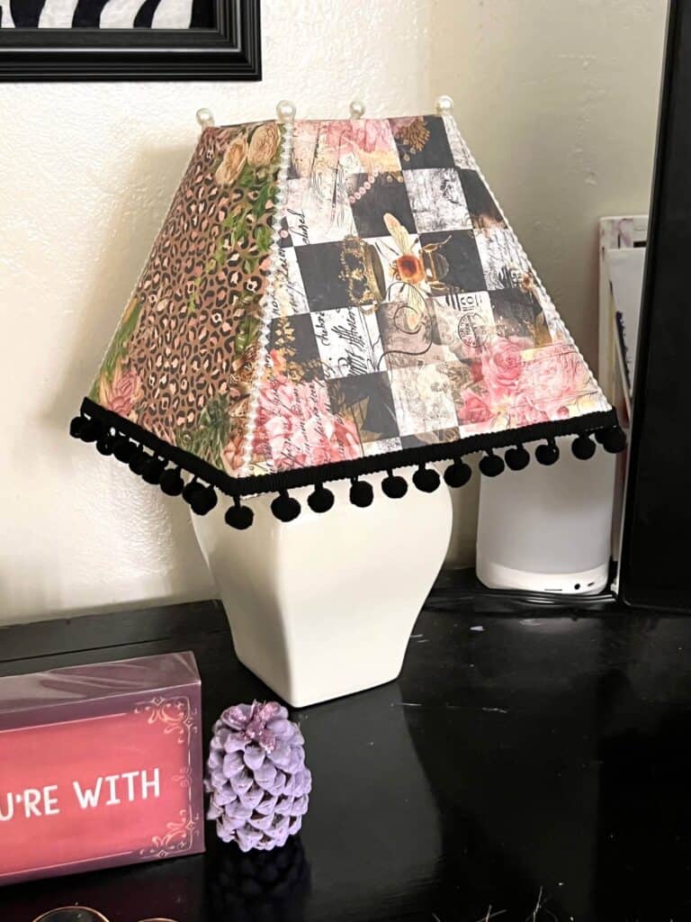 Thrift Store Lamp Flip. Makeover of a white lampshade with rice paper printables decoupaged onto the shade with black pom pom trim around the bottom and pearl strips up the side with pearl beads.