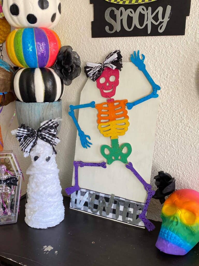 The completed foam cone mummy staged and decorated with a rainbow skeleton and rainbow skull on a book shelf.