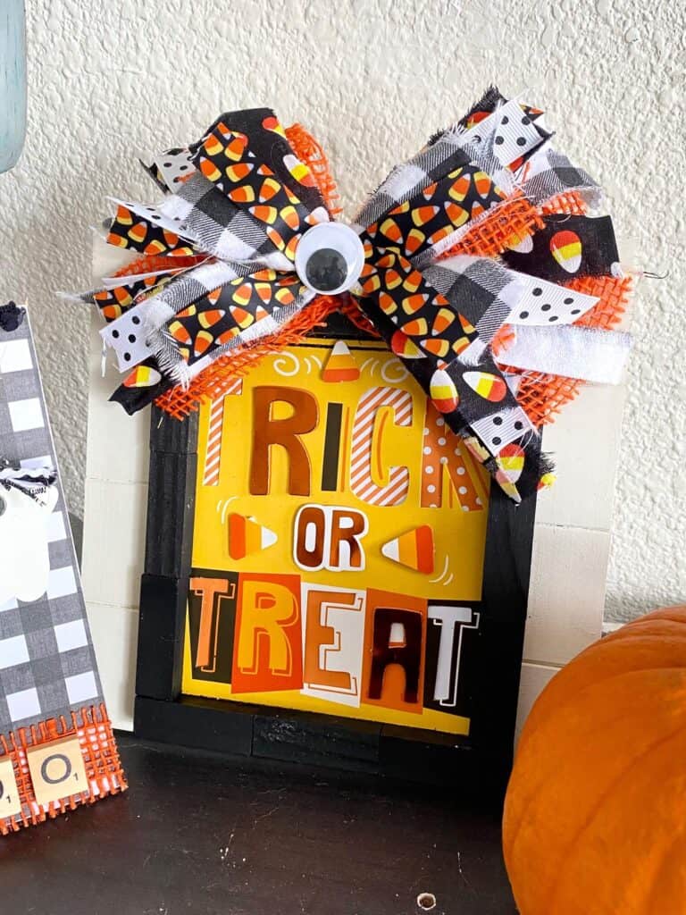 DIY Dollar Tree Trick or Treat Frame made with a Halloween card and a huge messy bow with candy corn, orange, black, and a jumbo googly eye in the center.