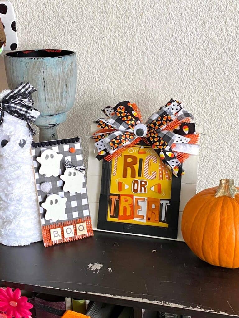 A foam cone mummy, a mini Boo ghost decor, the Dollar Tree Trick or Treat frame with messy bow and a large pumpkin sitting on a bookcase.