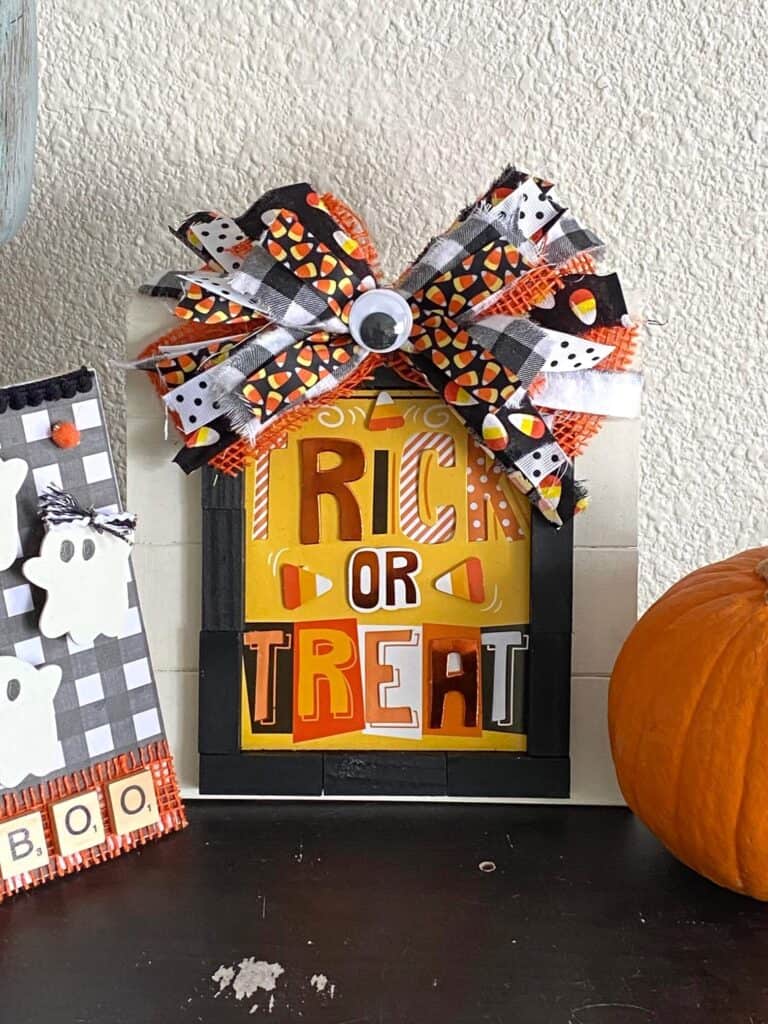 DIY Dollar Tree Trick or Treat Frame made with a Halloween card and a huge messy bow with candy corn, orange, black, and a jumbo googly eye in the center.