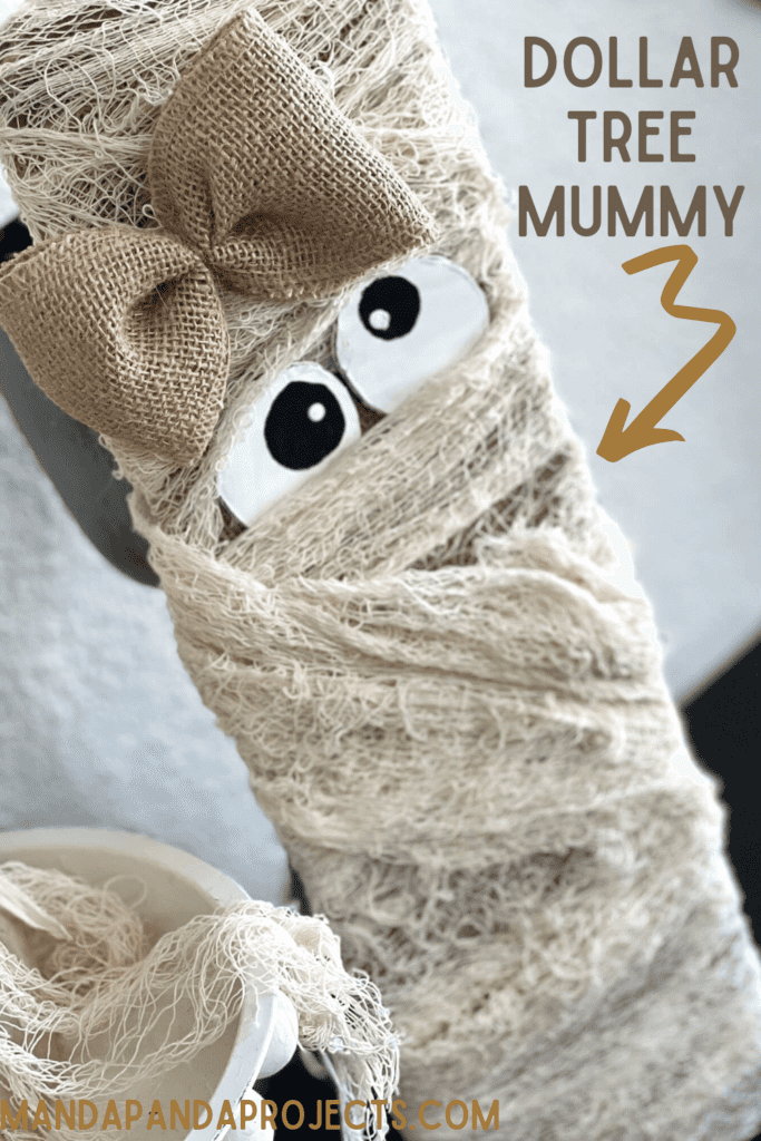 Dollar Tree Creepy Cheese Cloth Mummy Decor with burlap, a girly bow, cardboard wonky eyes on a long wood board for DIY Halloween decor on a budget.