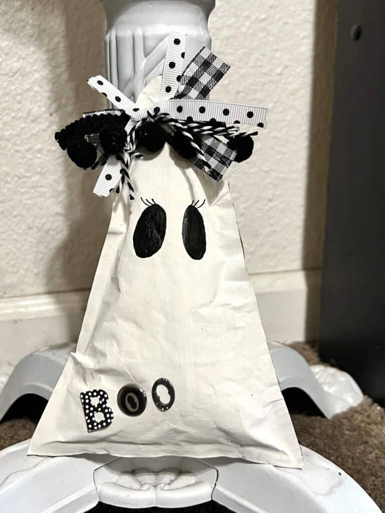 Girl Kraft paper ghost with a black and white bow on her head, black eyes with eyelashes, and the word "boo" with black, white and silver stickers.