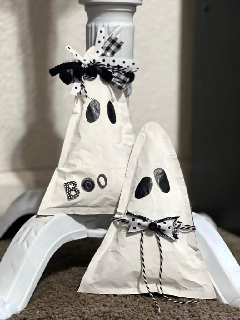 Kraft Paper Ghosts DIY easy and affordable Halloween decor. Boy and girl triangle shaped ghosts with black and white bow and bow tie and the word BOO, with 2 black eyes and no mouth.