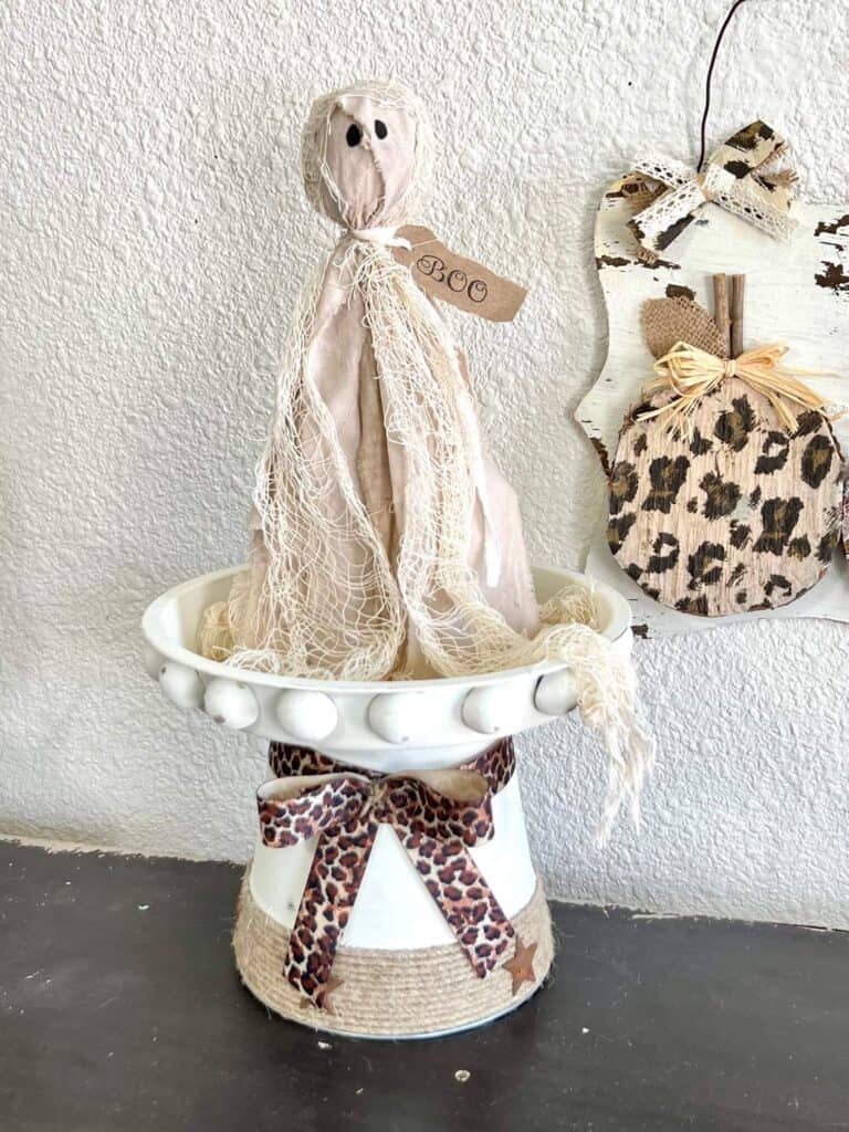 DIT Primitive Halloween Rag Ghost sitting on a farmhouse white riser large half wood beads and a leopard print bow.
