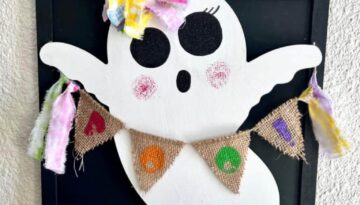 Dollar Tree Wooden Ghost with a Burlap Rainbow BOO Banner with colored fabric tassels, a rainbow messy bow, and big black sparkly ghost eyes with eyelashes, for cute DIY Halloween decor on a budget.
