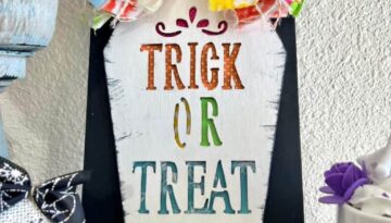 Dollar Tree Trick or Treat Wooden Coffin makeover craft for a DIY Halloween decor piece in a colorful rainbow theme with a big messy bow, cross bones, and a spider on a black background.